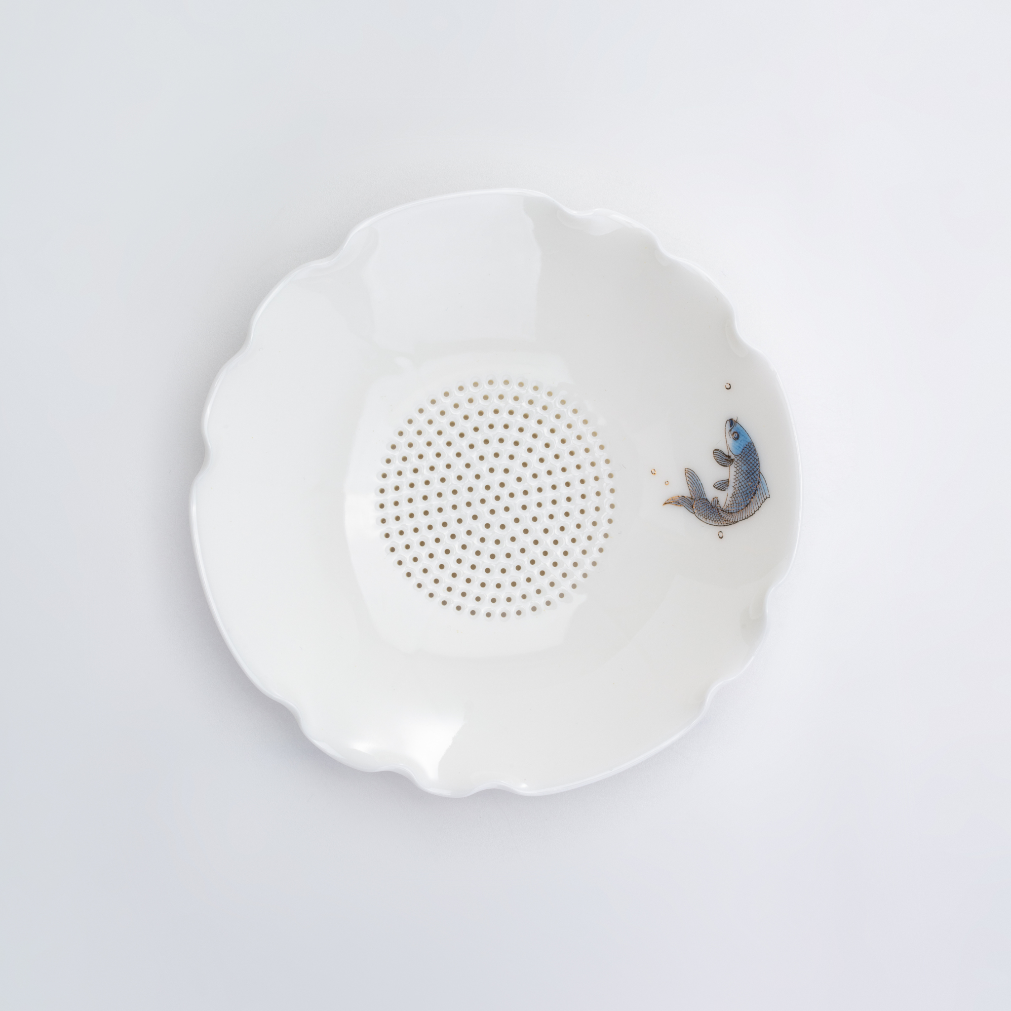 White ceramic tea filter with decorative edge on a light gray background