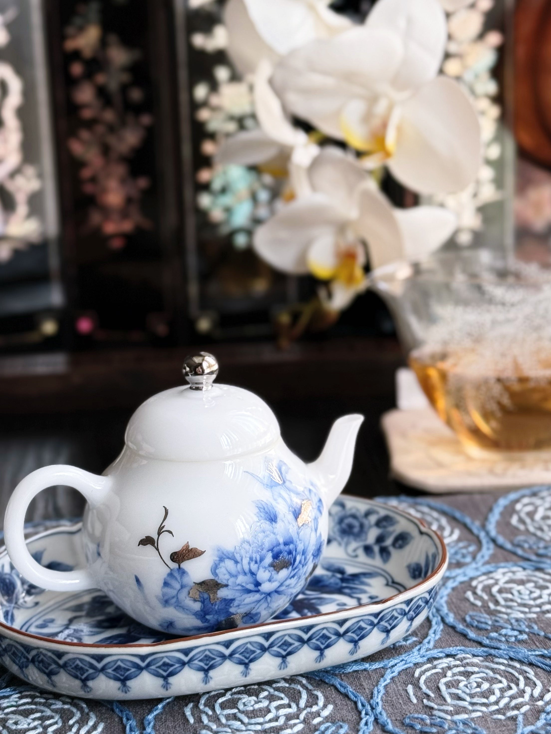 Traditional Chinese teapot with floral design on a matching tray, set against a decorative background.