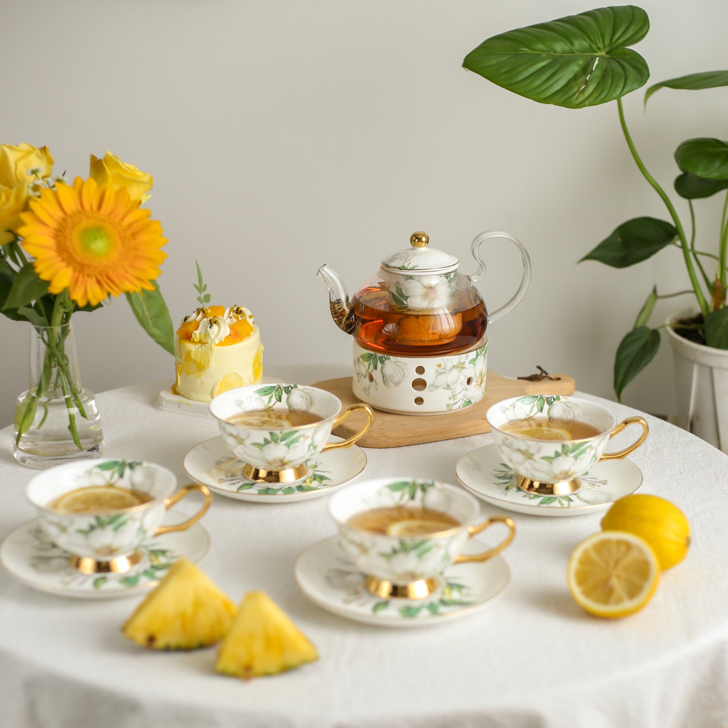 Tea set with cups, saucers, and a teapot on a table with lemons and flowers.