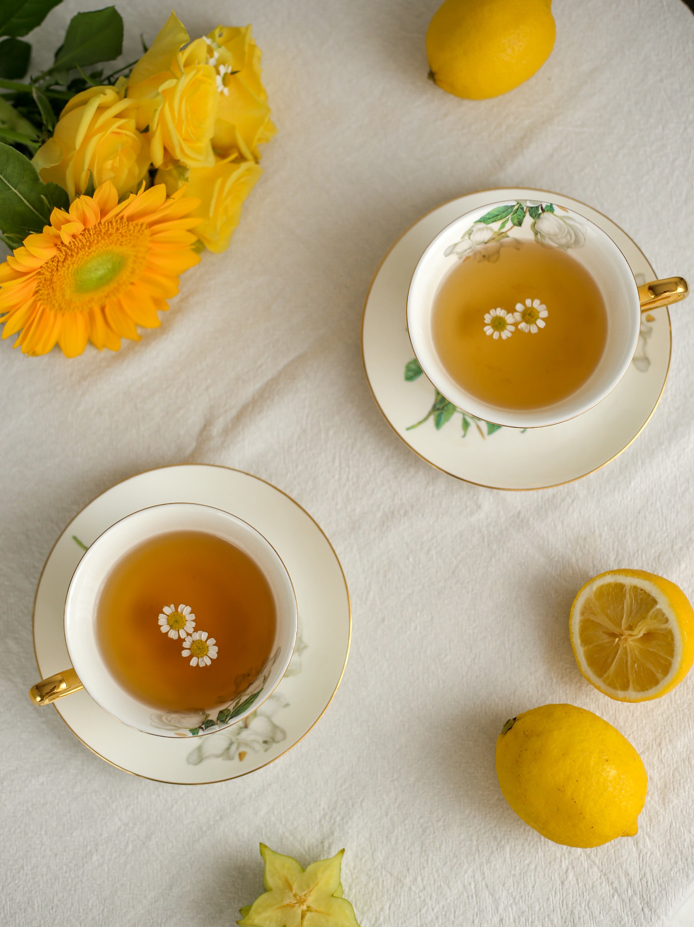 Two cups of tea with lemon slices and flowers on a white surface