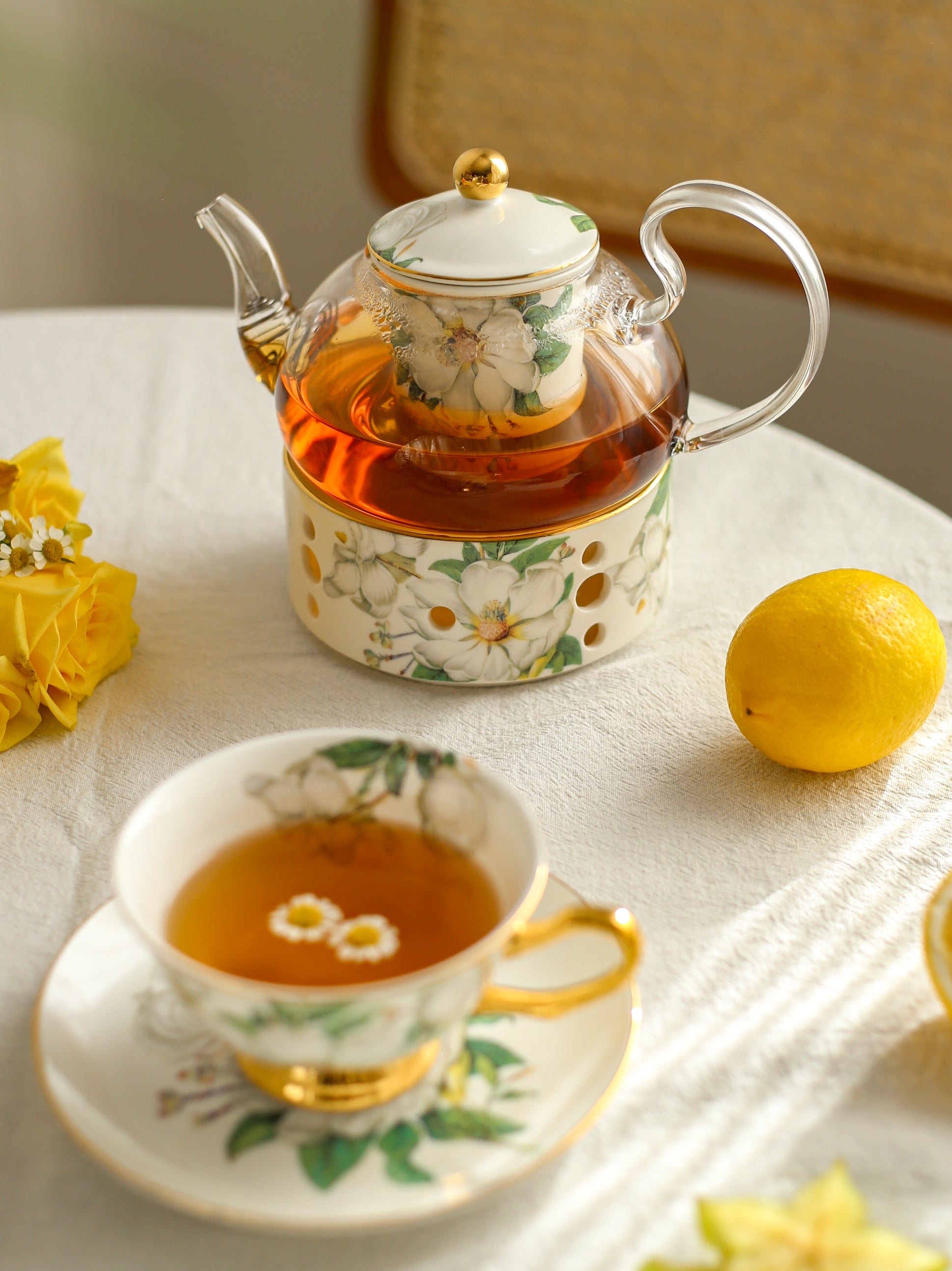 Tea set with floral design on a table with lemon and flowers.