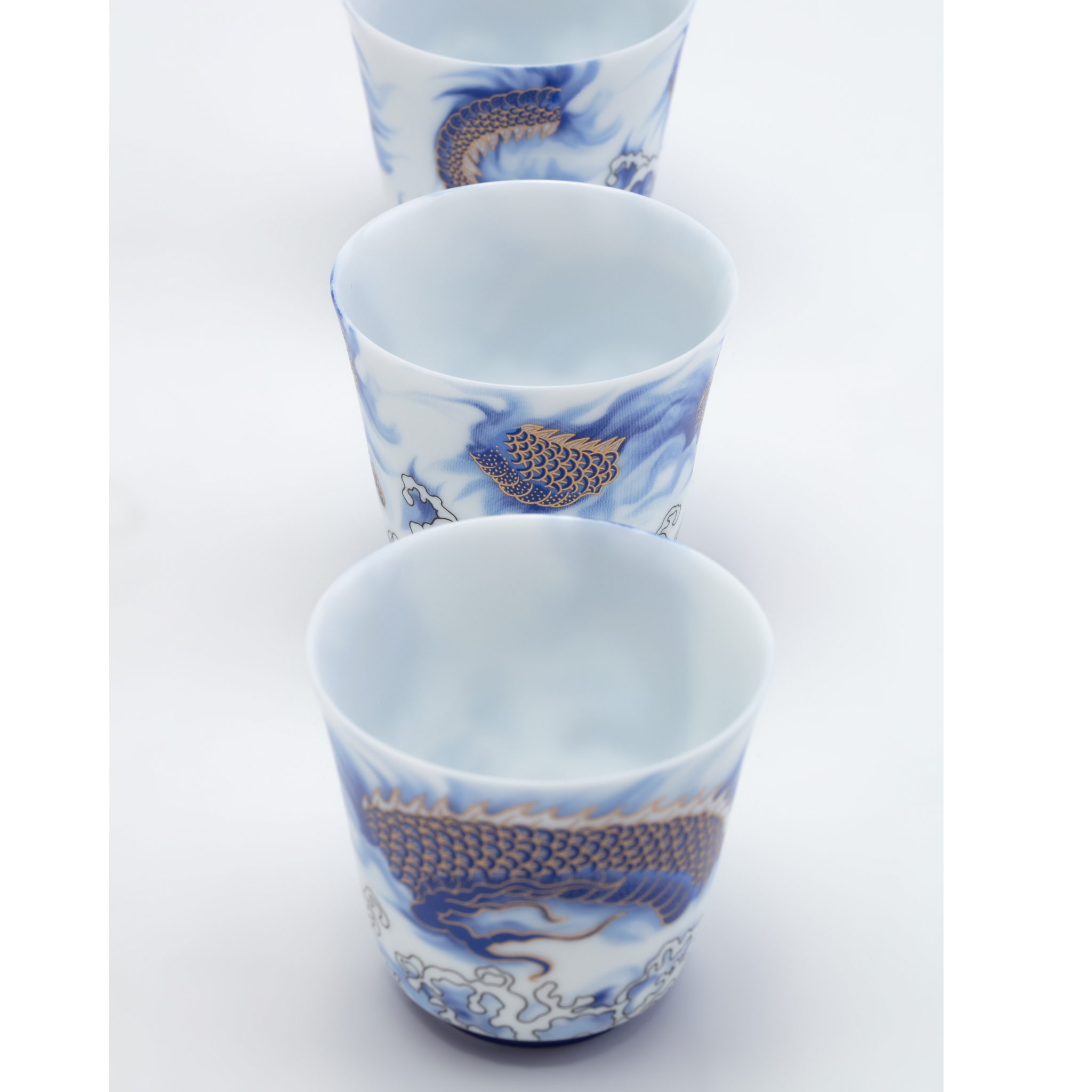 Set of three ceramic cups with blue and white dragon designs on a white background