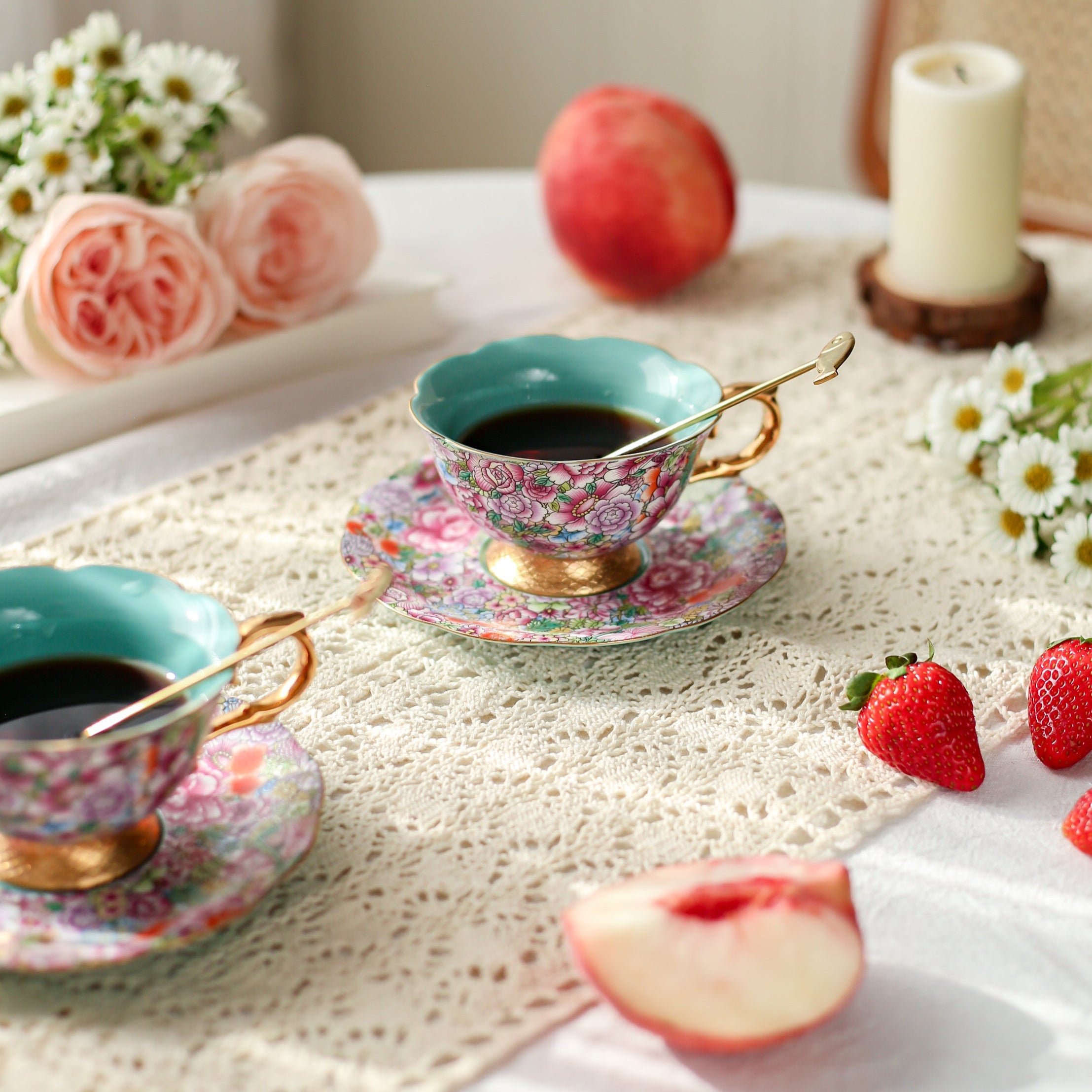 Teacups with floral patterns on a table with fruits and flowers