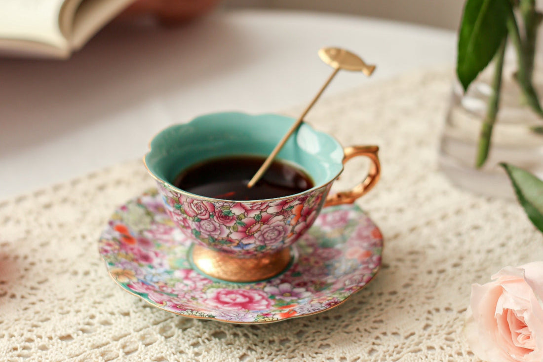 Teacup with floral design on a lace tablecloth, accompanied by strawberries and a book.