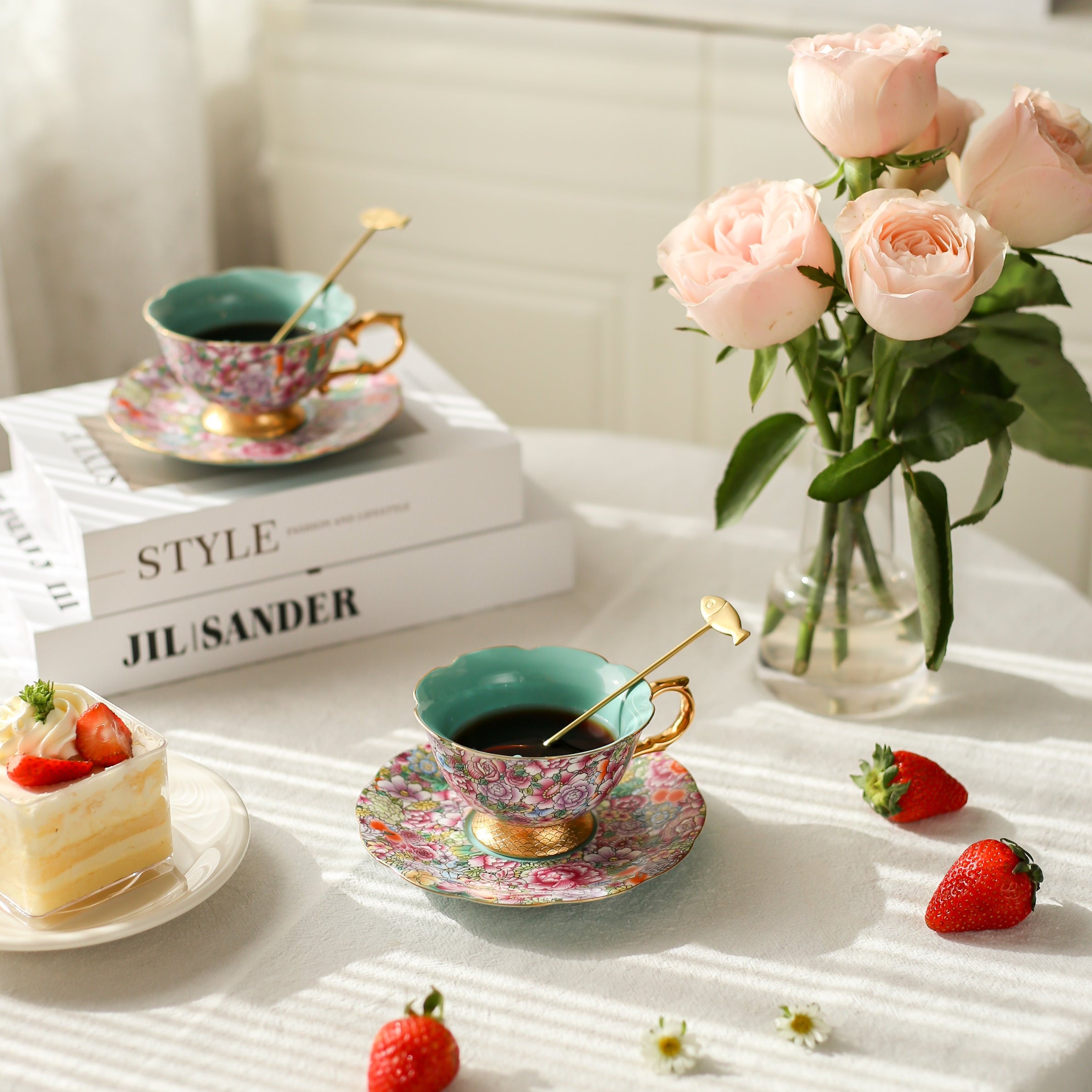 Tea set with teacups, saucers, and strawberries on a table with a vase of flowers.