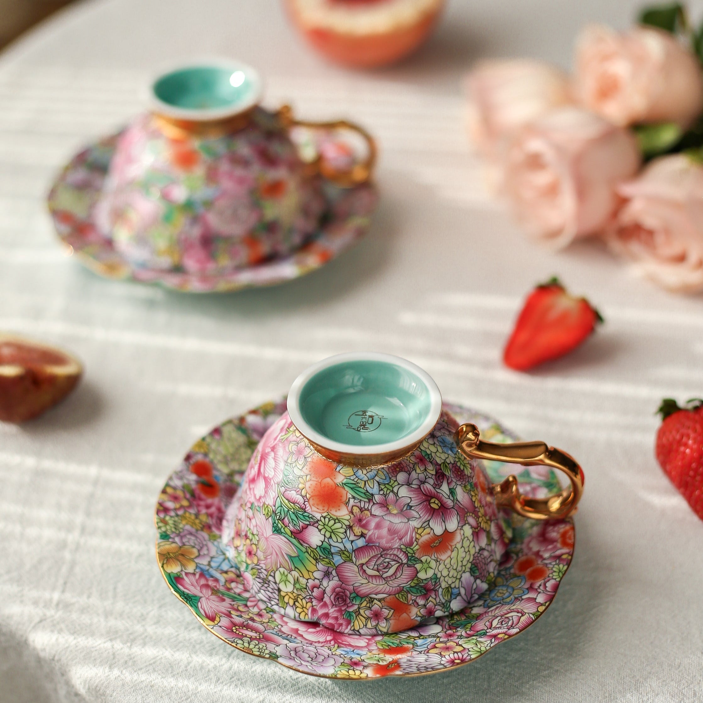 Floral teacup and saucer set on a white surface with strawberries and peaches.
