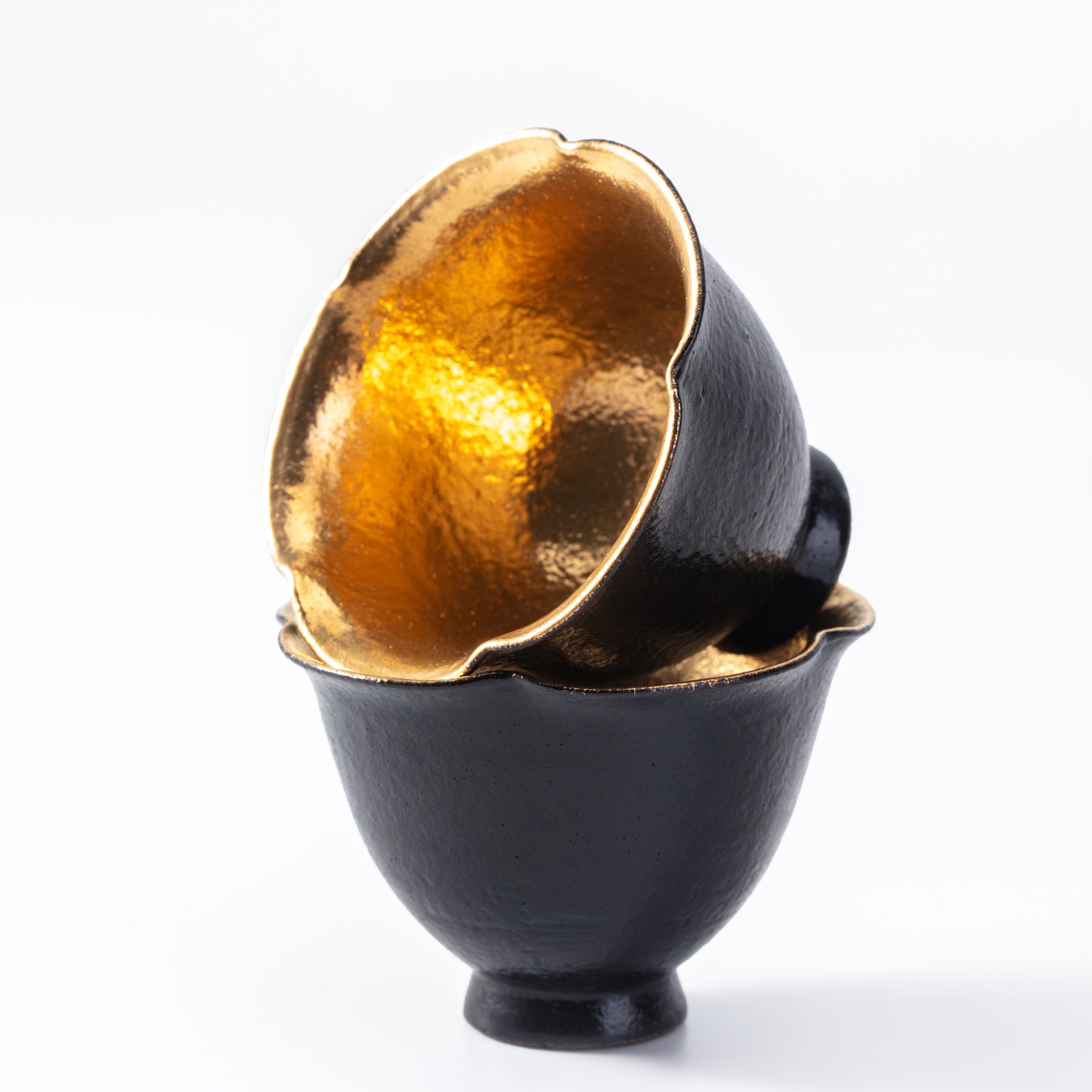Black ceramic egg cups with gold interior on a white background