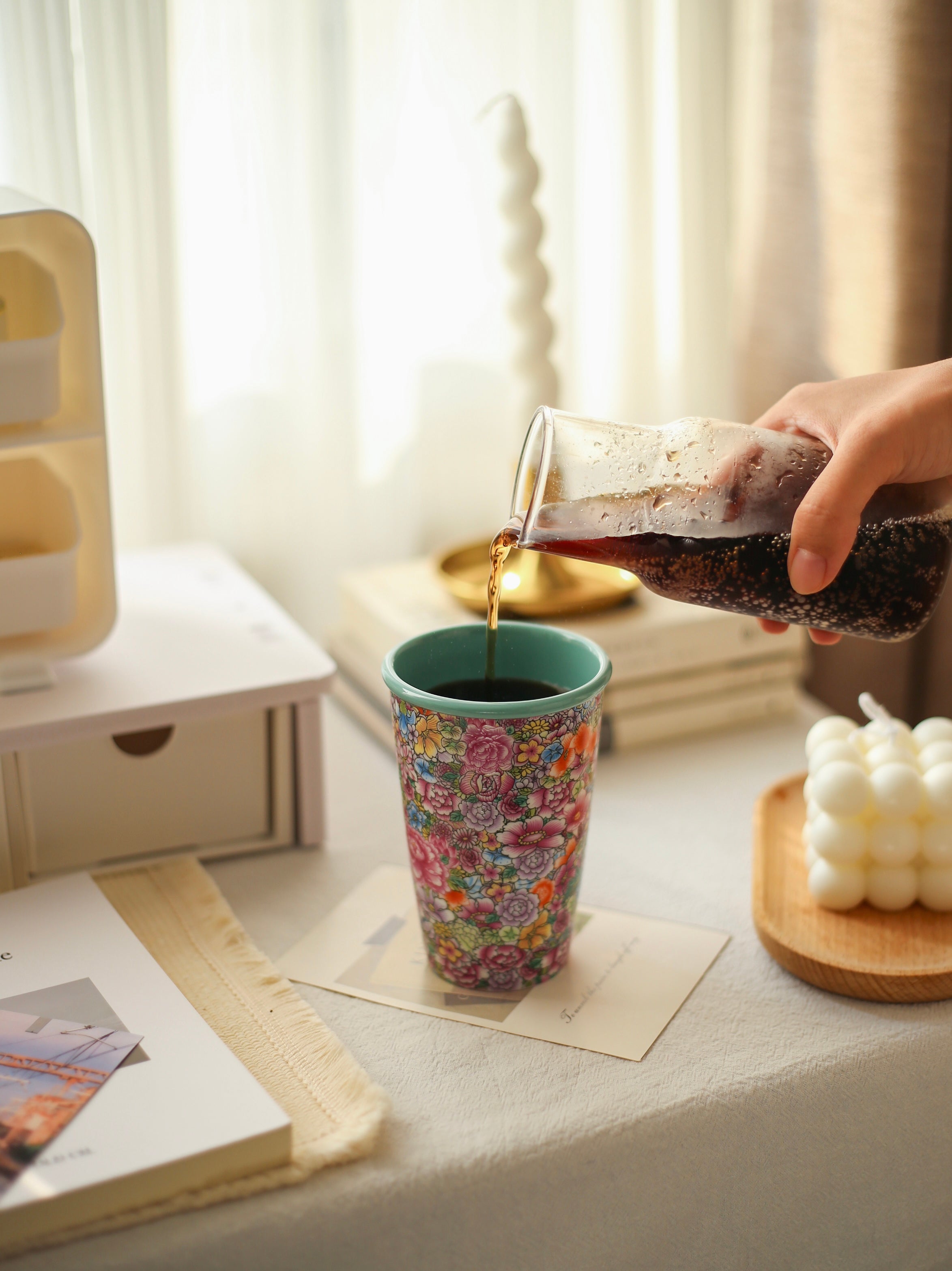 Person pouring coca cola into a colorful Falangcai mug on a table.