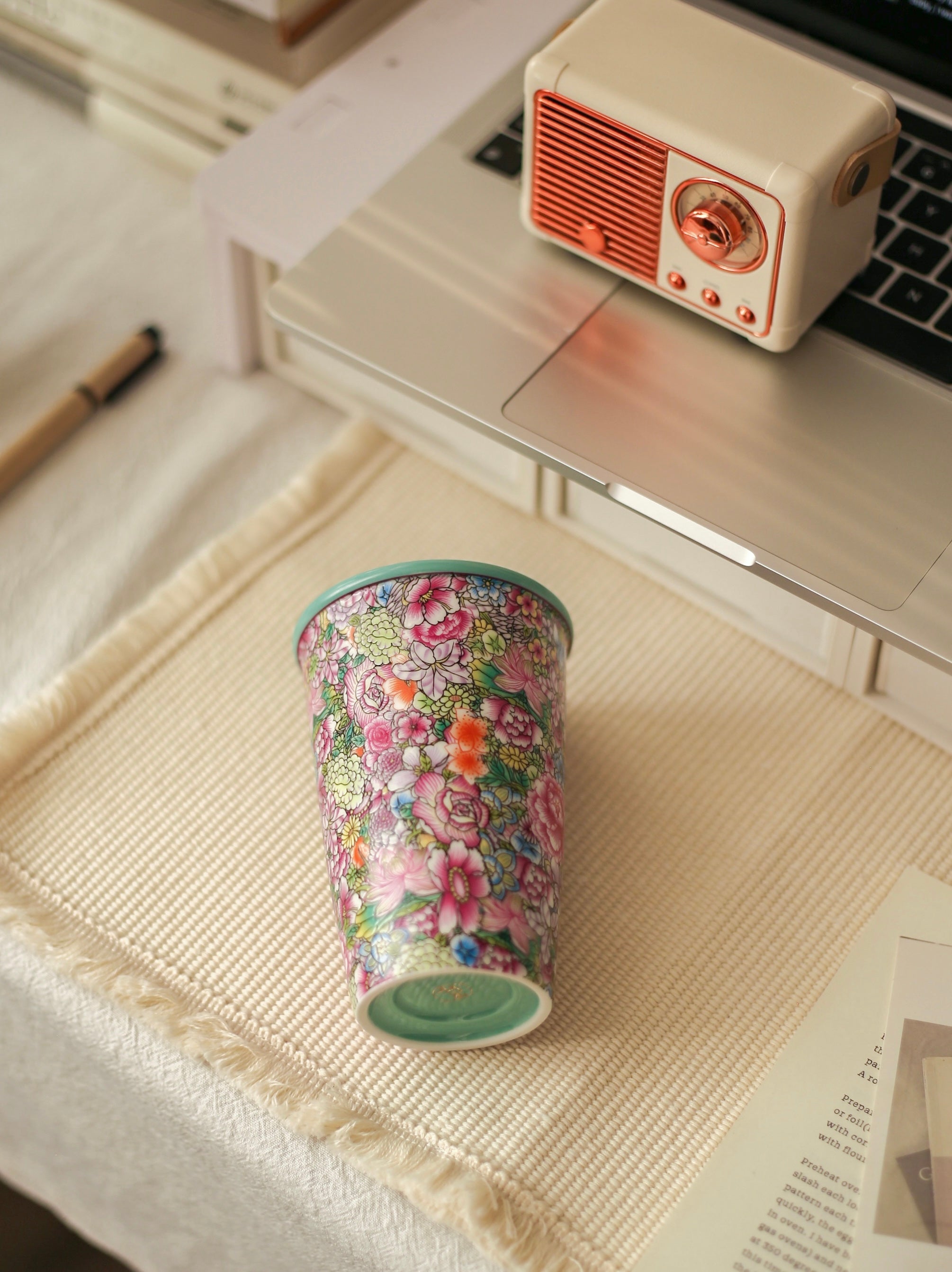 Floral-patterned Falangcai tumbler on a desk with a laptop and small radio.