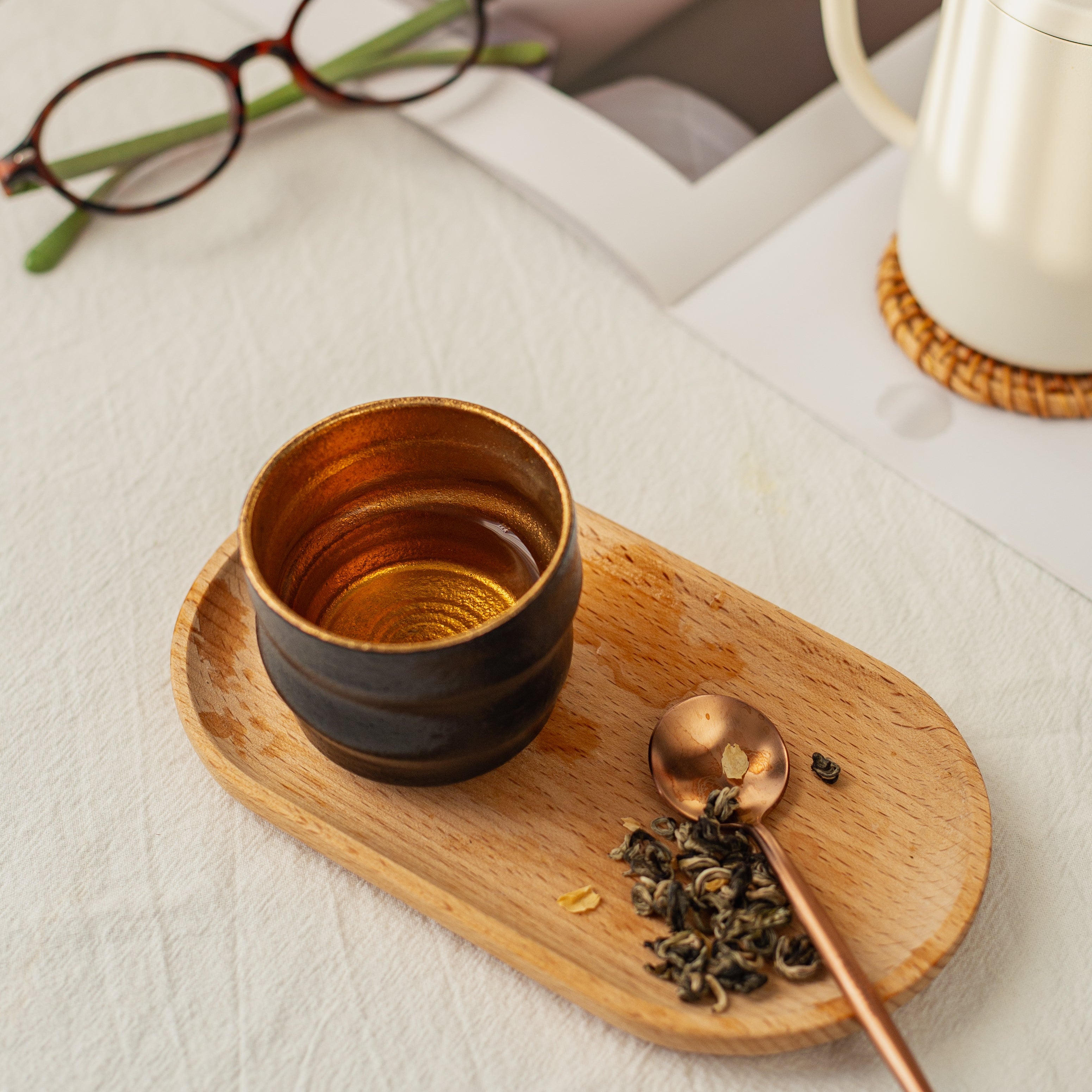 Tea cup, wooden tray, and teapot on a light surface with a magazine in the background.