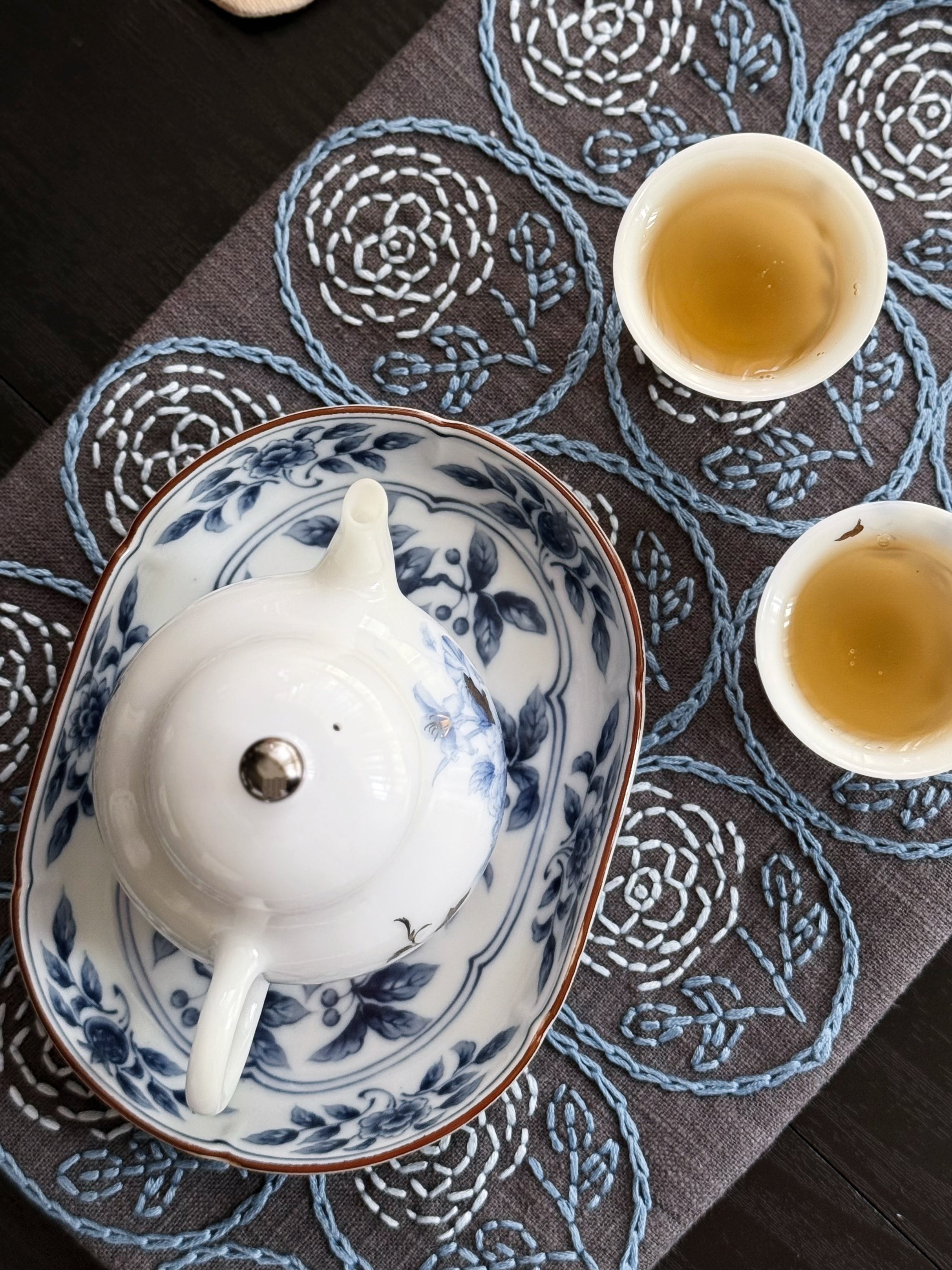 Tea set with a teapot and two cups on a decorative tablecloth.