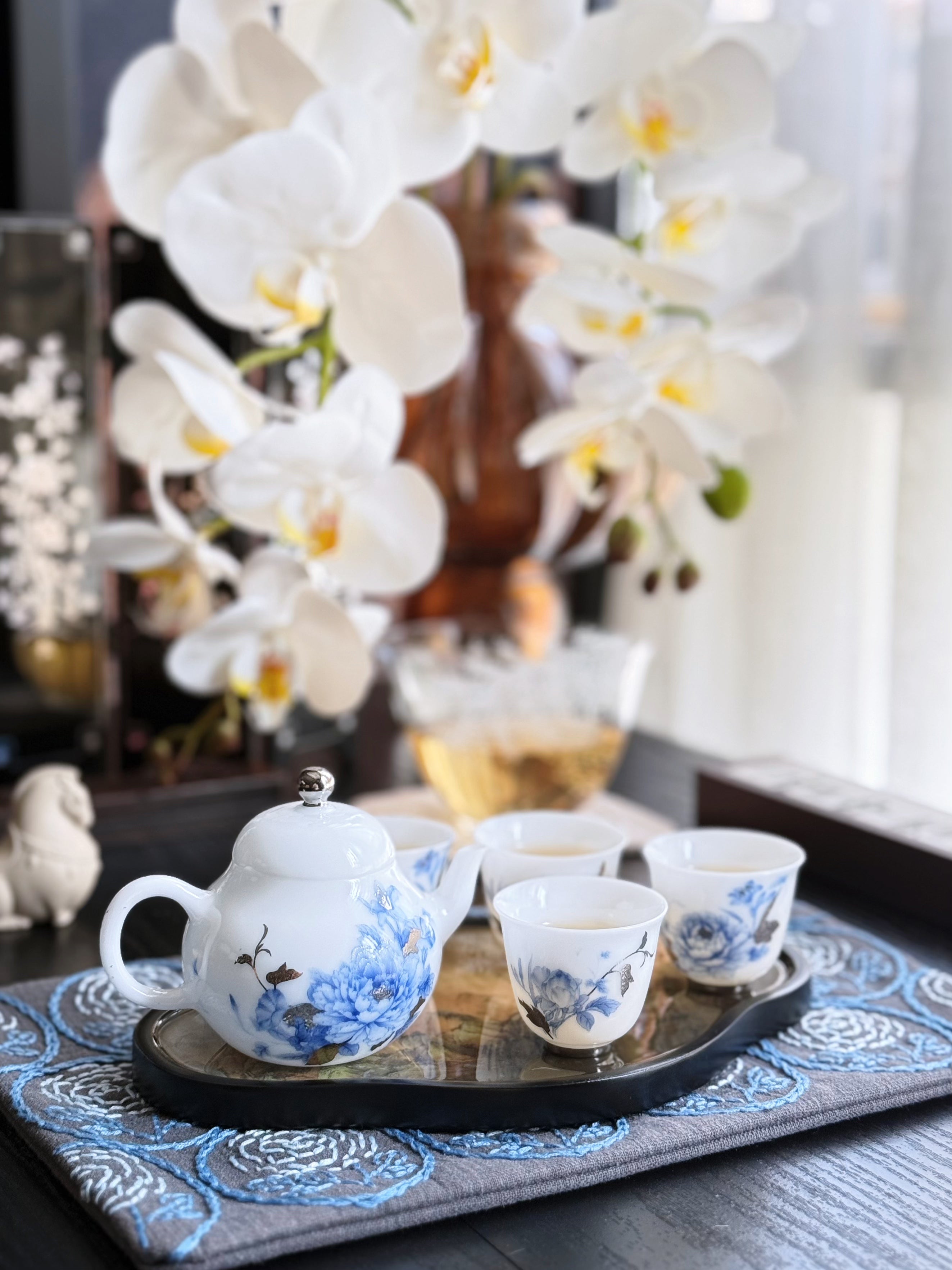 Tea set with floral design on a tray in front of white orchids