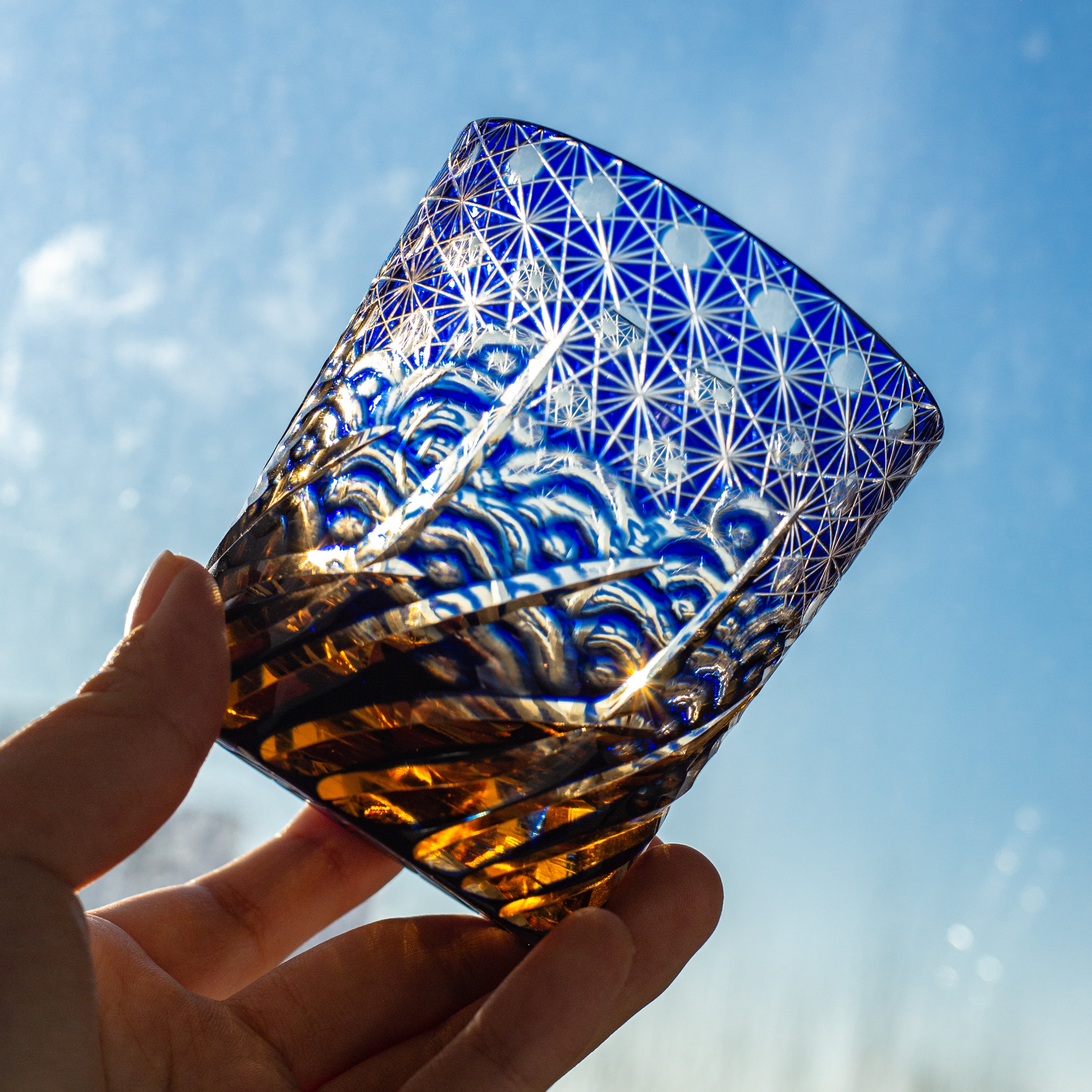 Hand holding a blue and white patterned Crystal Whiskey Glass against a blue sky.