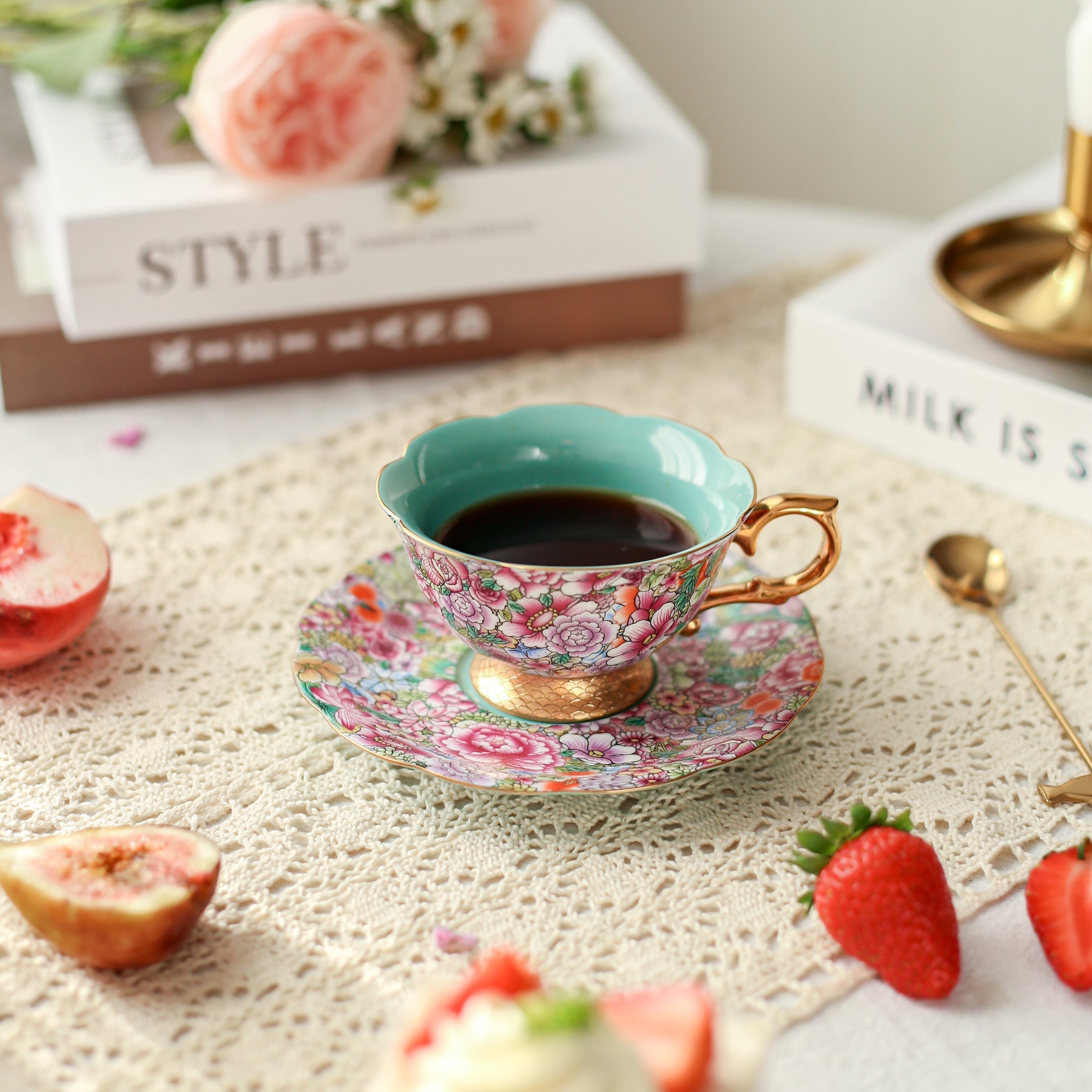Teacup with floral design on a table with strawberries and books in the background