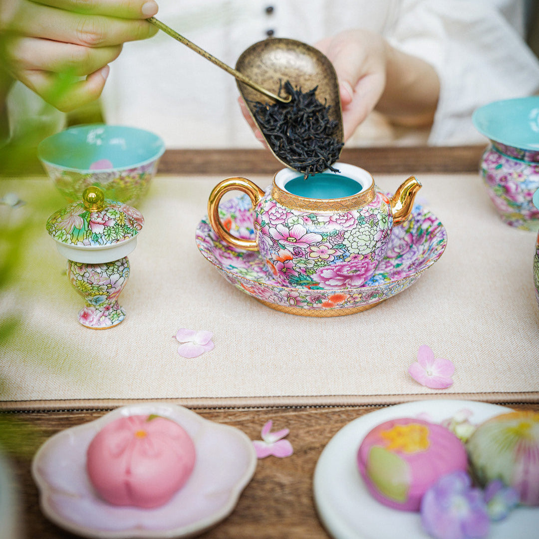 Tea ceremony with a teapot, tea leaves, and floral elements on a wooden table.