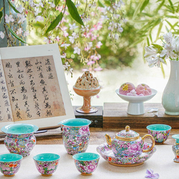 Tea set with floral cups on a wooden table outdoors, surrounded by greenery.